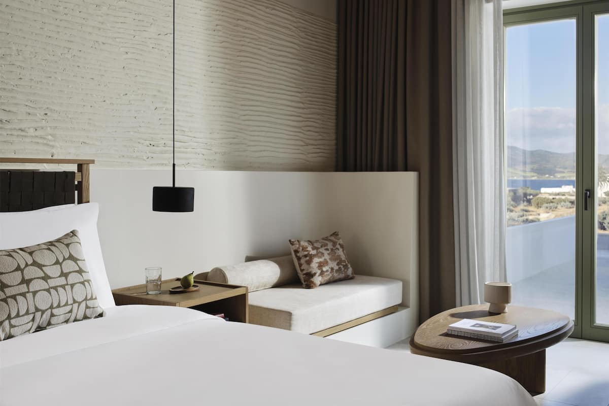 Une chambre d’hôtel avec un lit, un canapé, une petite table, une lampe et une vue sur l’extérieur.