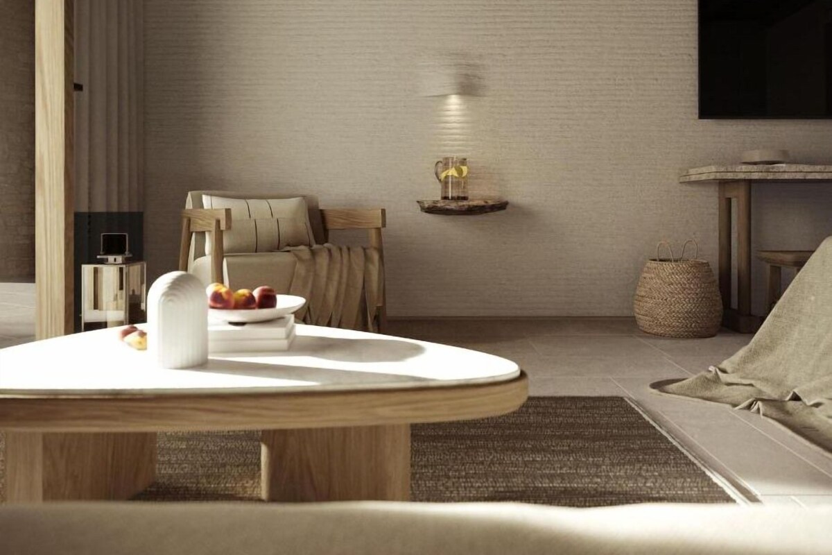 En moderne stue med et rundt træbord, en sofa, et tv ophængt på væggen og et lille sofabord med en lampe.