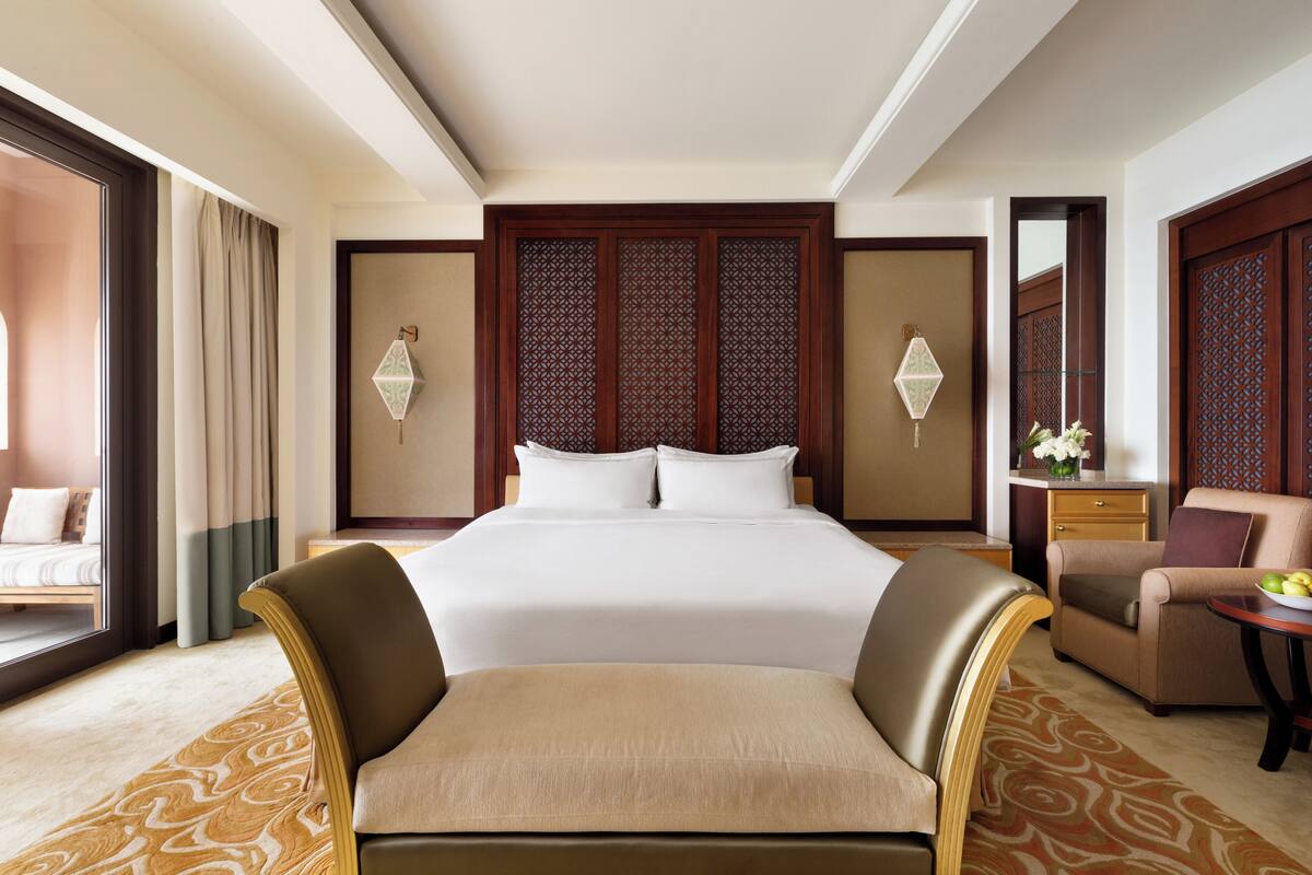 Une chambre d’hôtel avec un grand lit, deux tables de chevet avec des lampes, un canapé et une petite table avec des fruits.