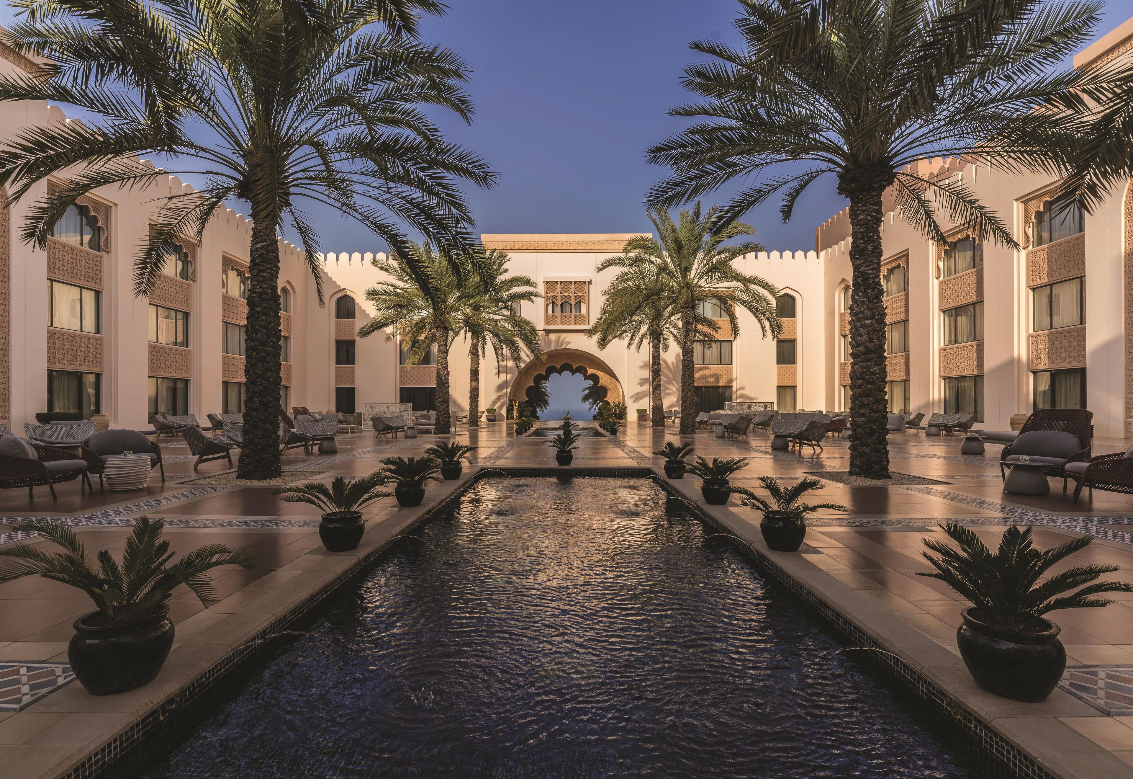 A hotel lobby with a central water feature, palm trees, and seating areas.