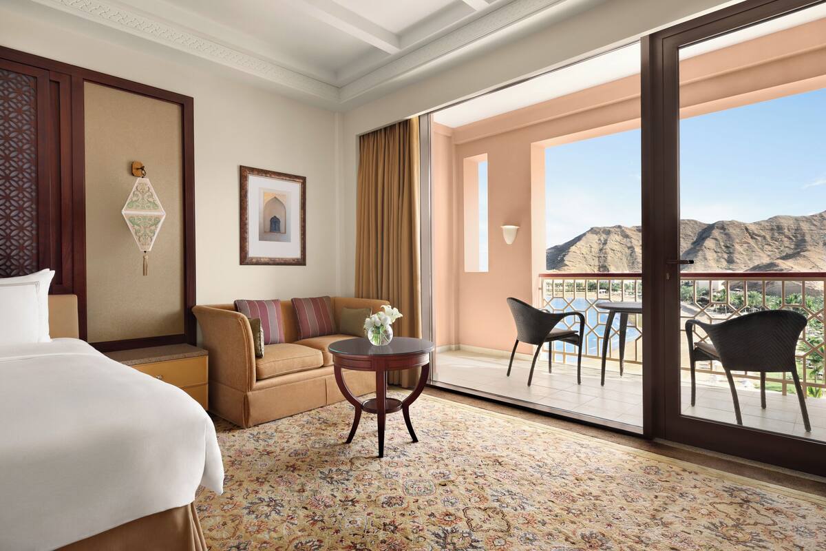 Une chambre d’hôtel comprenant un lit, un canapé, une table ronde et un balcon avec des chaises et une table.