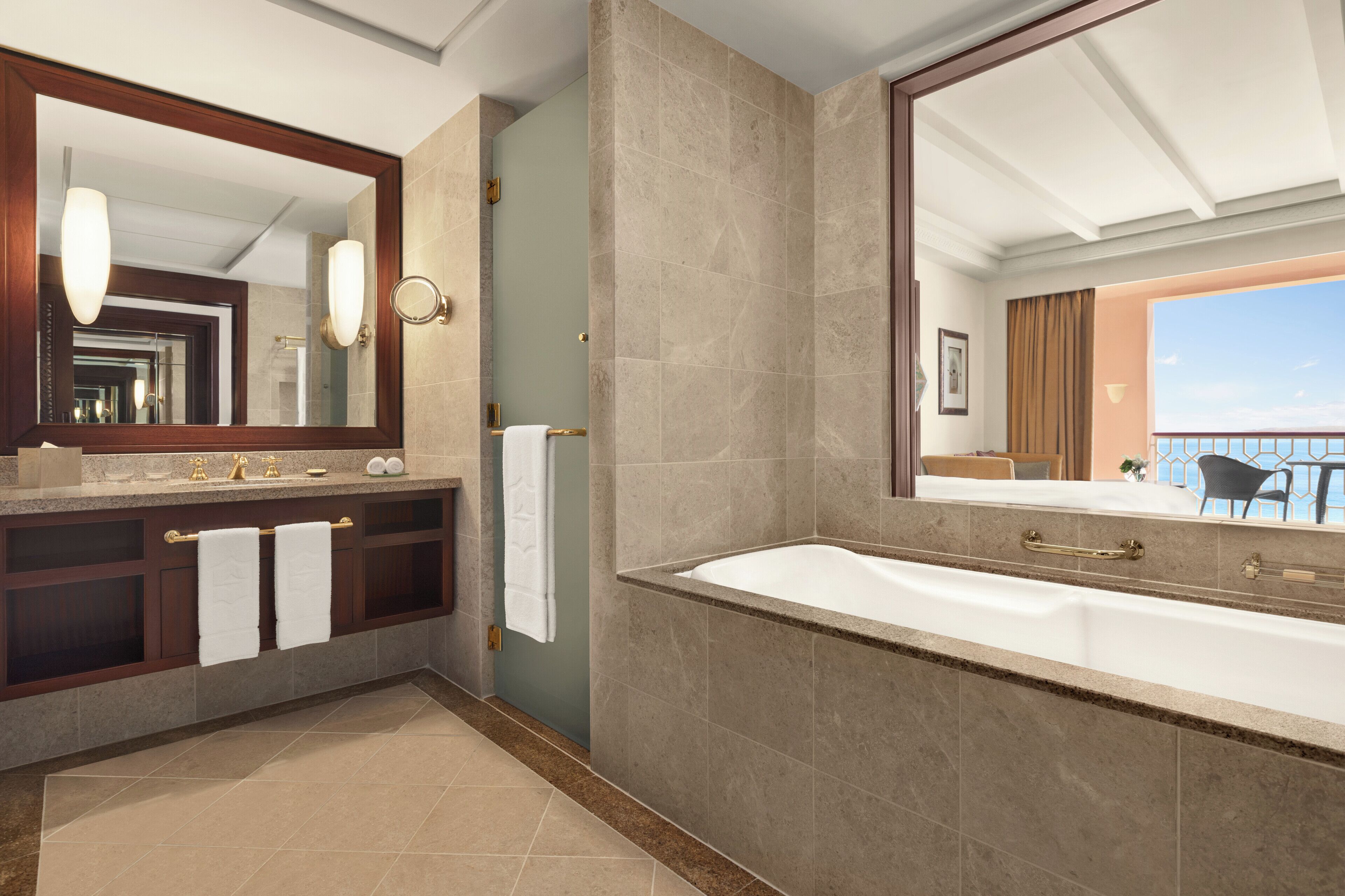 A modern bathroom with a large bathtub, a vanity with a mirror, and a view of the balcony.