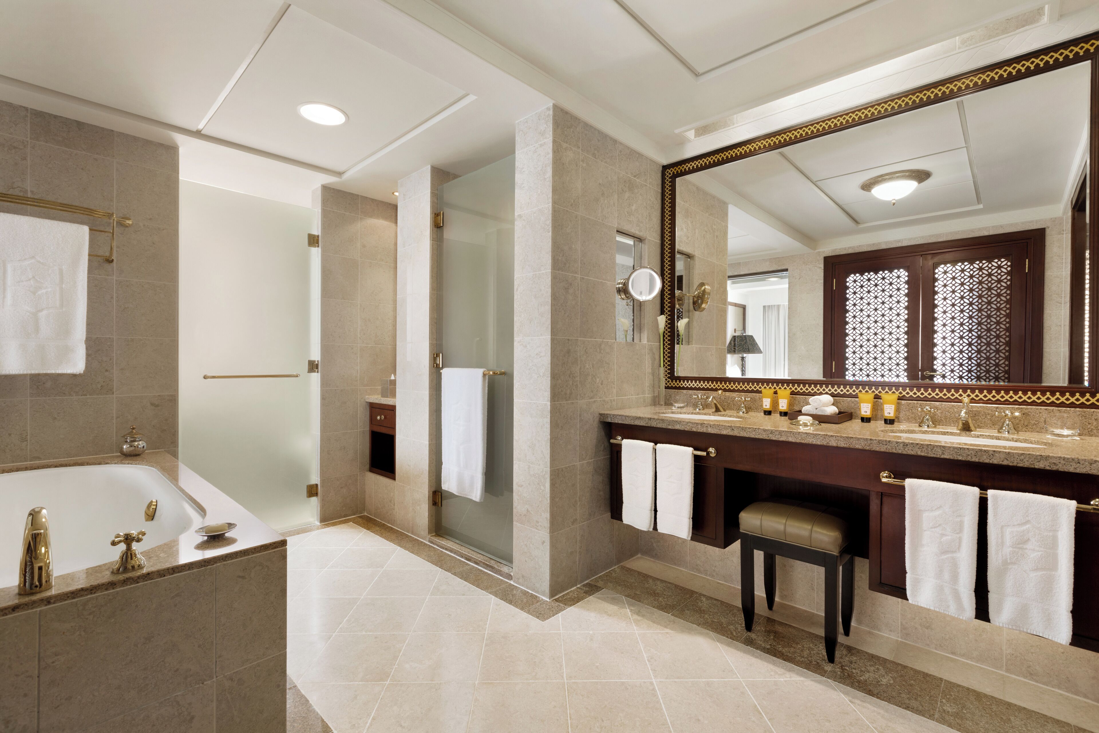 A modern bathroom with a large mirror, a bathtub, a shower, and a vanity with toiletries.