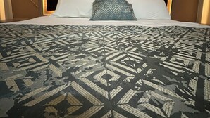 A bed with a patterned bedspread, a headboard with a light fixture, and wall-mounted artwork. - Luxe Nest (Luxor)