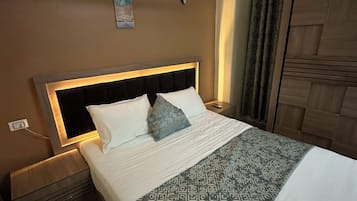 A neatly made bed with a patterned bedspread, a headboard with built-in lighting, a bedside table, and a wall-mounted clock.