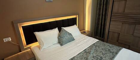 A neatly made bed with a patterned bedspread, a headboard with built-in lighting, a bedside table, and a wall-mounted clock.