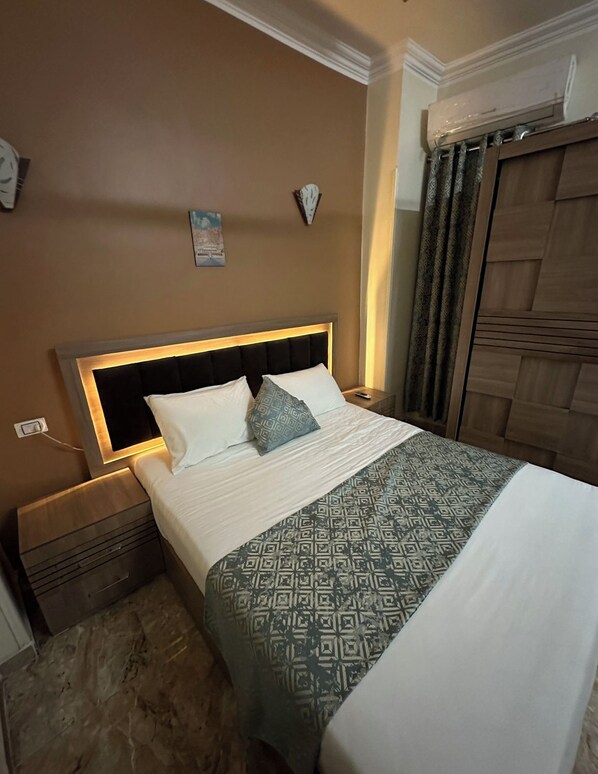 A neatly made bed with a patterned bedspread, a headboard with built-in lighting, a bedside table, and a wall-mounted clock.