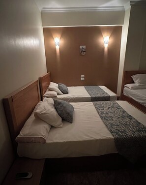 A hotel room with two single beds, each with a wooden headboard, a bedside table, and a small bedside lamp. - Luxe Nest (Luxor)
