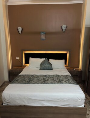 Una cama bien hecha con una colcha estampada, cabecero con iluminación integrada y dos relojes de pared.