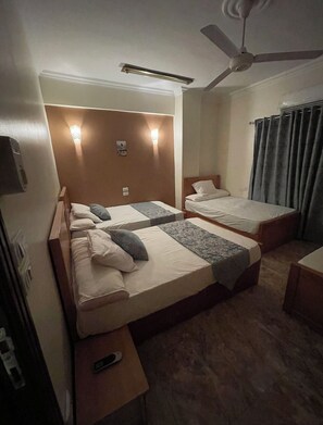 A hotel room with two single beds, a ceiling fan, and bedside lamps.