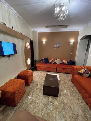 Una sala de estar con un sofá anaranjado grande, otomanas a juego, un televisor de pantalla plana, una araña y una chimenea.