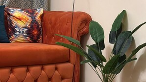 A corner of a room with a tufted orange sofa, a patterned pillow, and a potted plant with large green leaves. - Luxe Nest (Luxor)