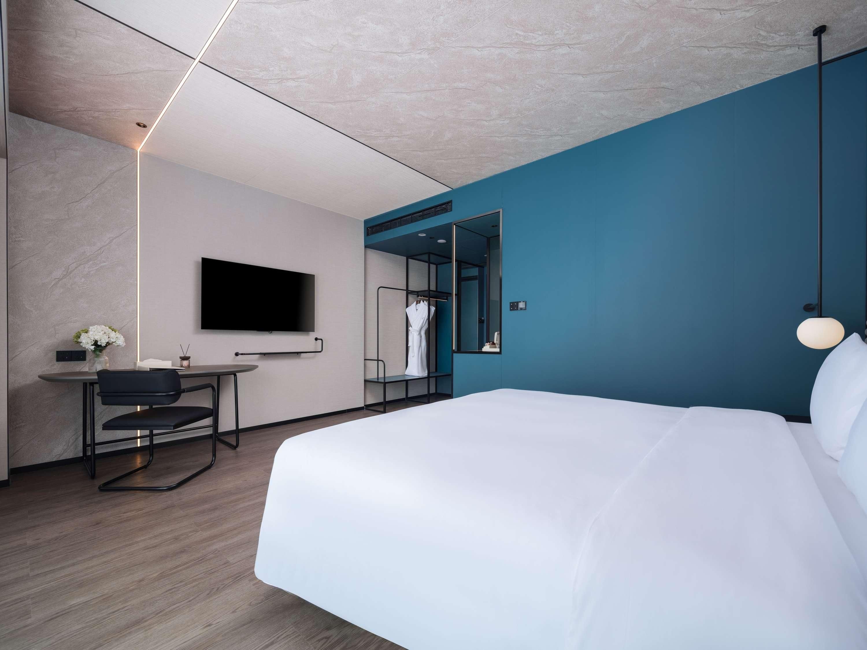 Una habitación de hotel moderna con una cama grande, un escritorio con silla, un televisor de pantalla plana y un espejo.