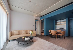 Un salon moderne avec un canapé beige, une table basse et un coin repas avec des chaises orange.
