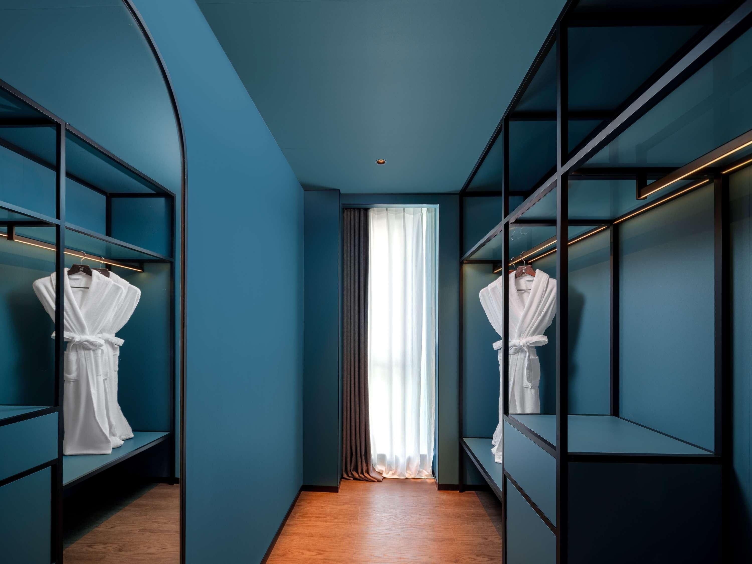 Ein moderner Hotelgang mit türkisfarbenen Wänden, Holzböden und integrierten Regaleinbauten mit weißen Bademänteln.