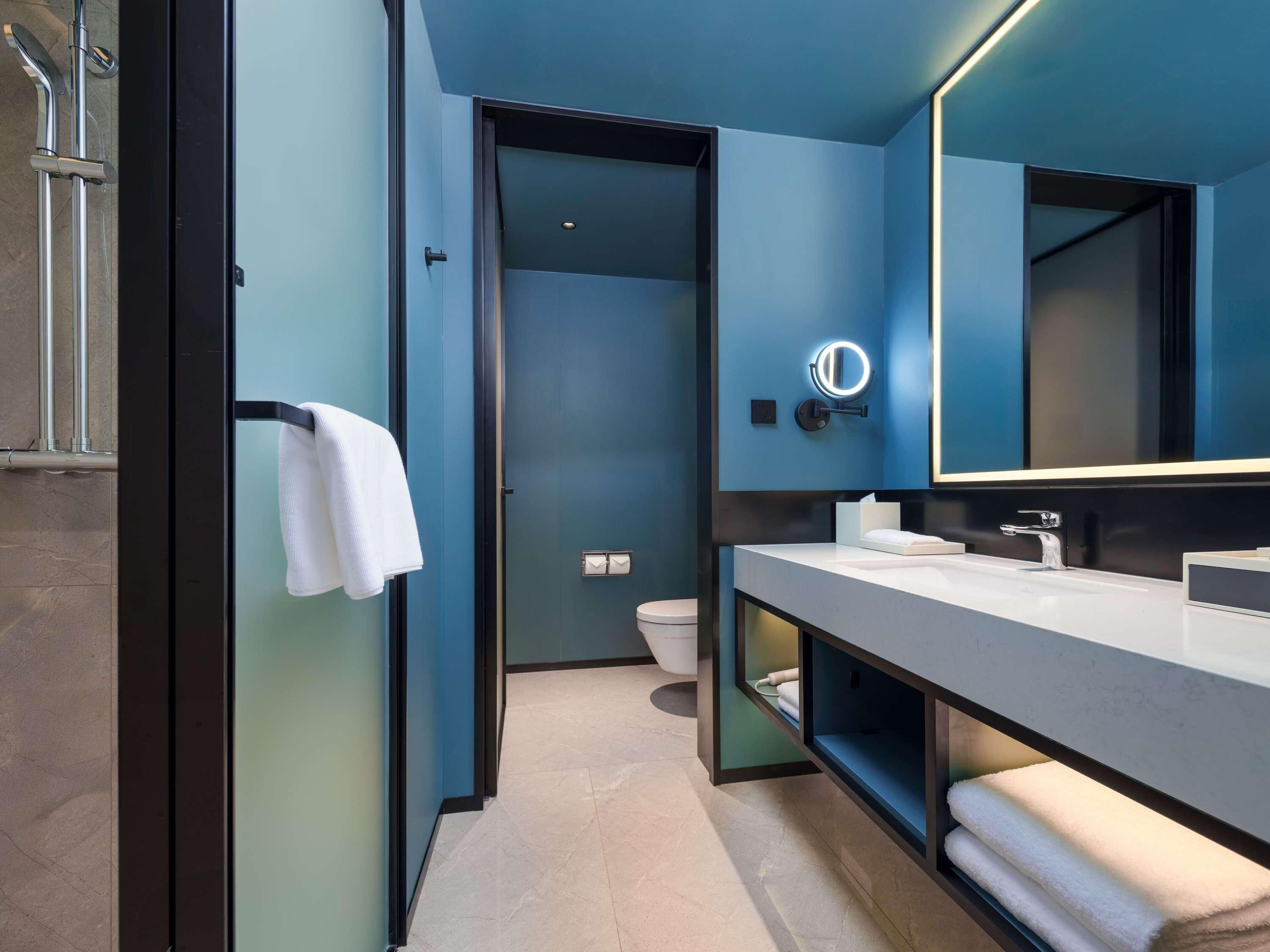A modern bathroom with a dark blue wall, a large mirror, a white towel hanging on a rack, and a toilet.