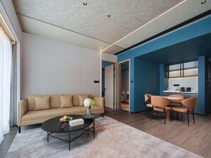 Ein modernes Wohnzimmer mit einem beigen Sofa, einem runden Couchtisch und einem Essbereich mit orangefarbenen Stühlen.