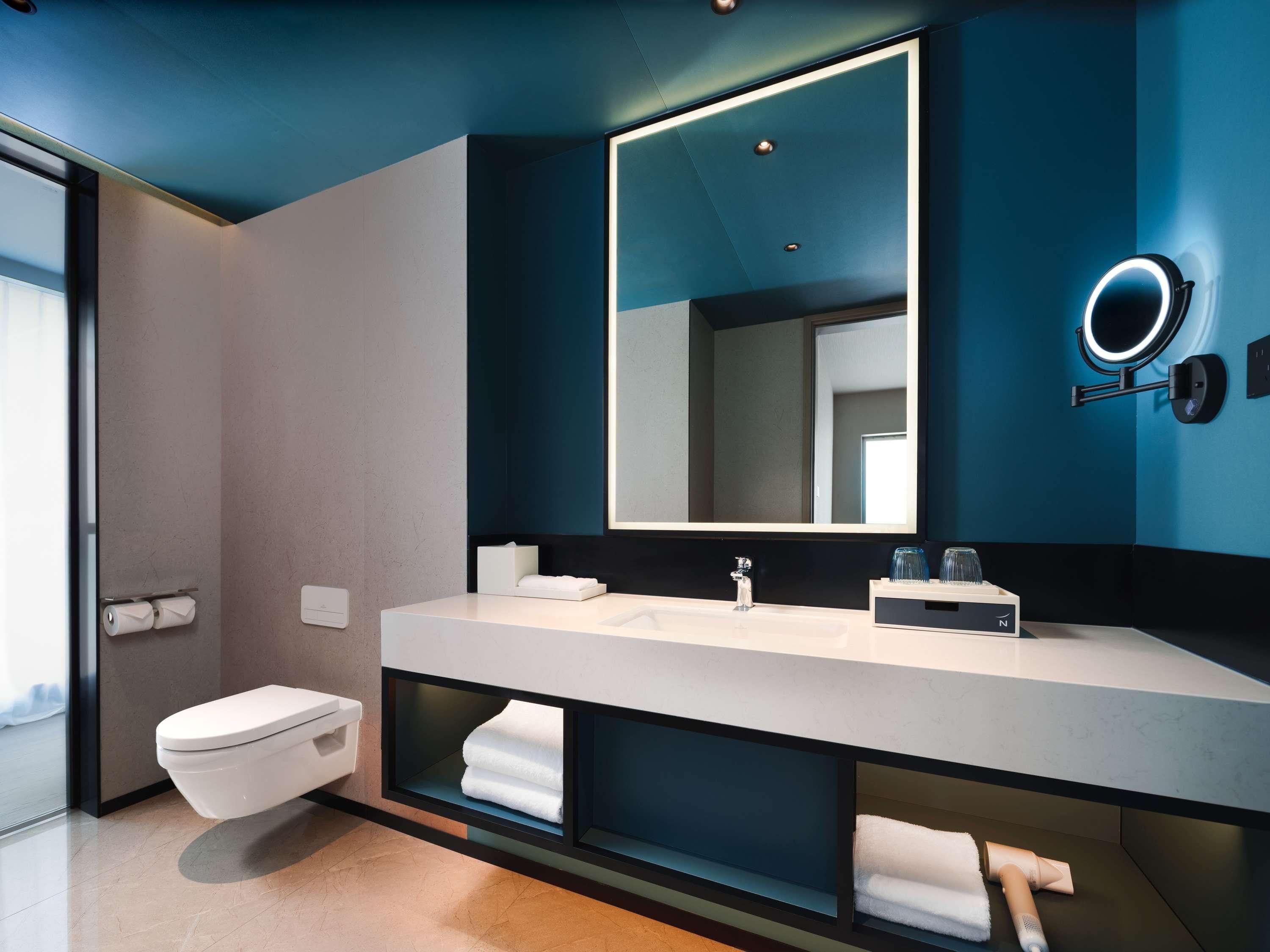 Une salle de bain moderne avec un grand miroir, un lavabo blanc et des étagères intégrées.