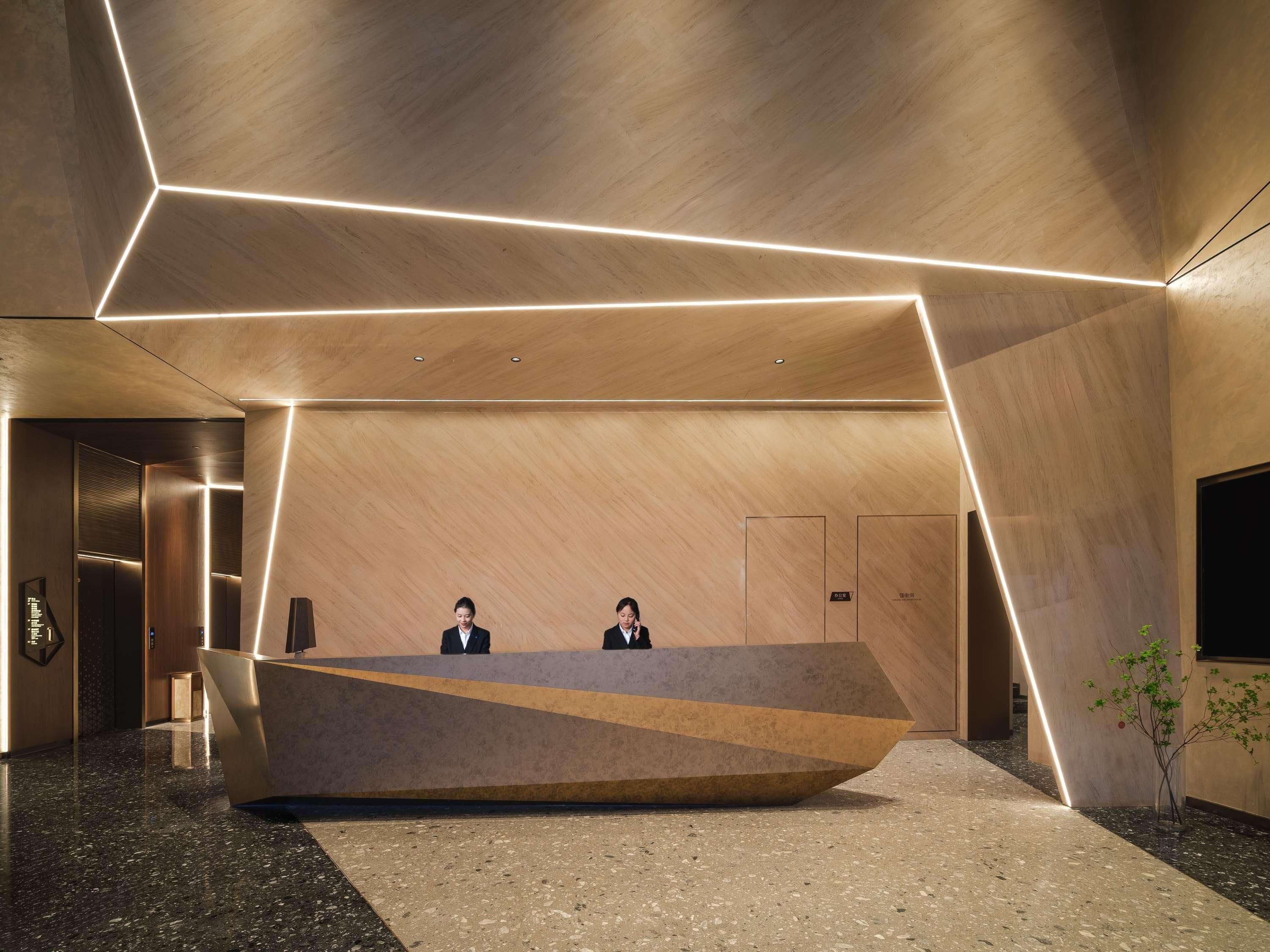 A modern reception area with a geometric reception desk, two staff members, and a minimalist design.