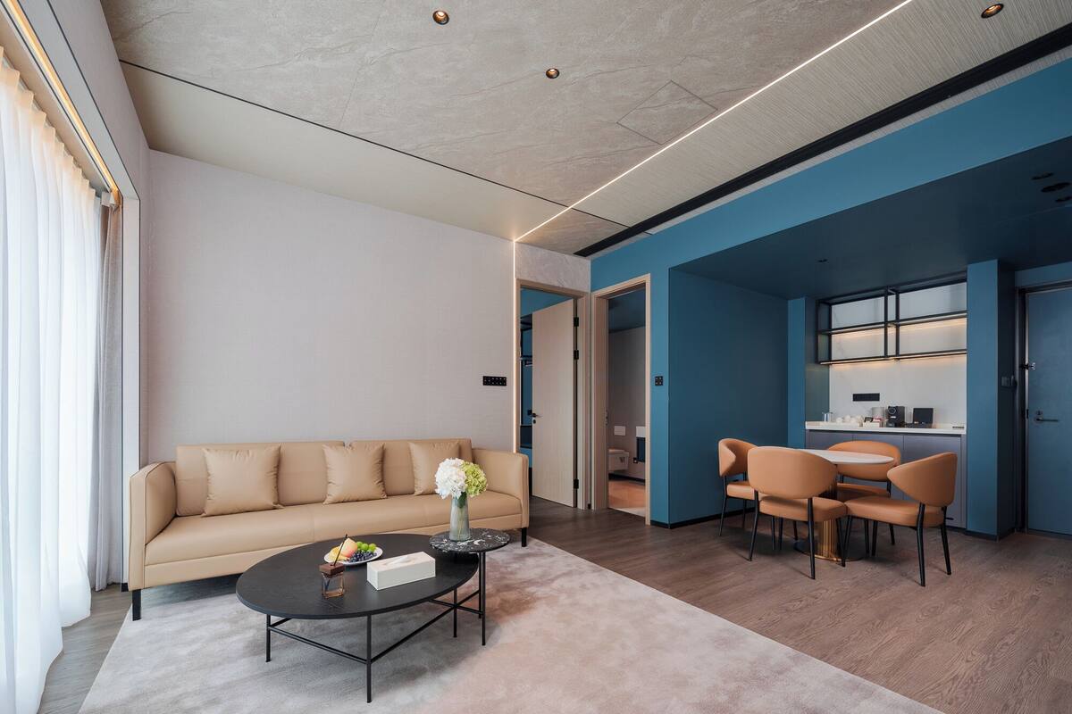 A modern living room with a beige sofa, a coffee table, and a dining area with orange chairs.