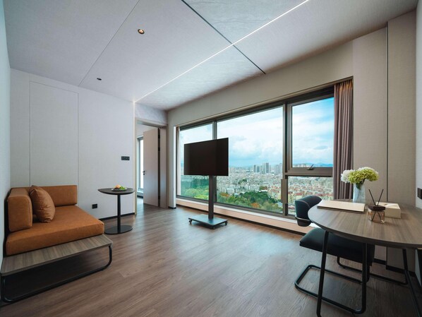 Une chambre d’hôtel moderne avec une grande fenêtre, un canapé, une petite table et un téléviseur.
