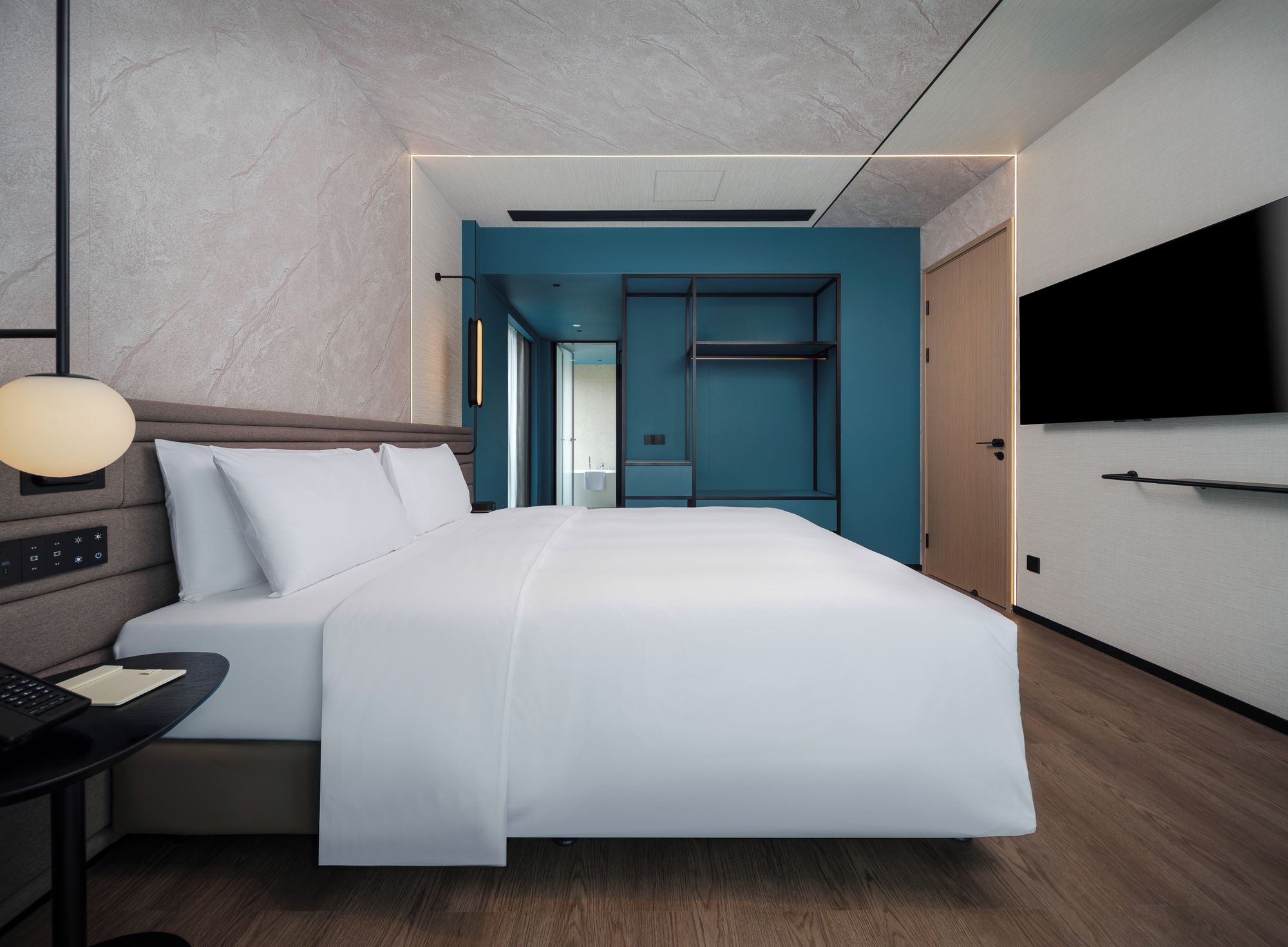 Ein modernes Hotelzimmer mit einem großen Bett, einem Schreibtisch mit Lampe und einem an der Wand befestigten Fernseher.