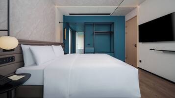 Ein modernes Hotelzimmer mit einem großen Bett, einem Schreibtisch mit Lampe und einem an der Wand befestigten Fernseher.