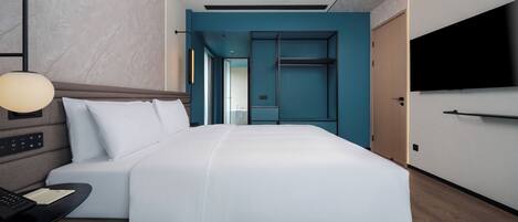 Habitación de hotel moderna con una cama grande, un escritorio con lámpara y un televisor montado en la pared.