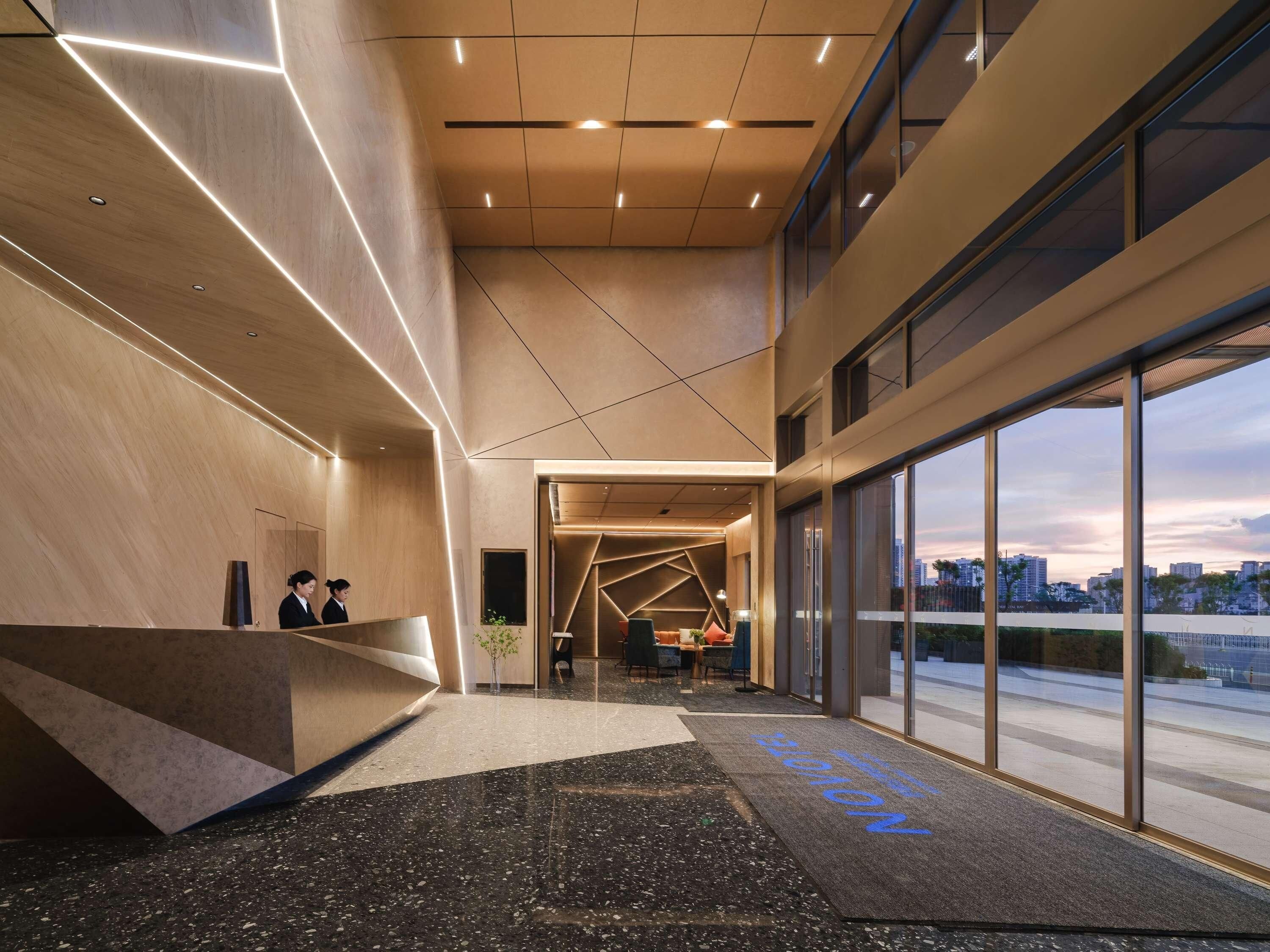 A modern hotel lobby with a reception desk, seating area, and large windows offering city views.