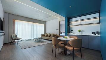 A modern living room with a sofa, a dining table with chairs, and a large window with blinds.