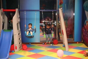 A children's play area with a swing set, a slide, and a colorful floor. - Tulip Inn Majan Hotel (Salalah)