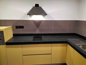 A kitchen with a black countertop, stainless steel sink, and yellow cabinets. - Tulip Inn Majan Hotel (Salalah)