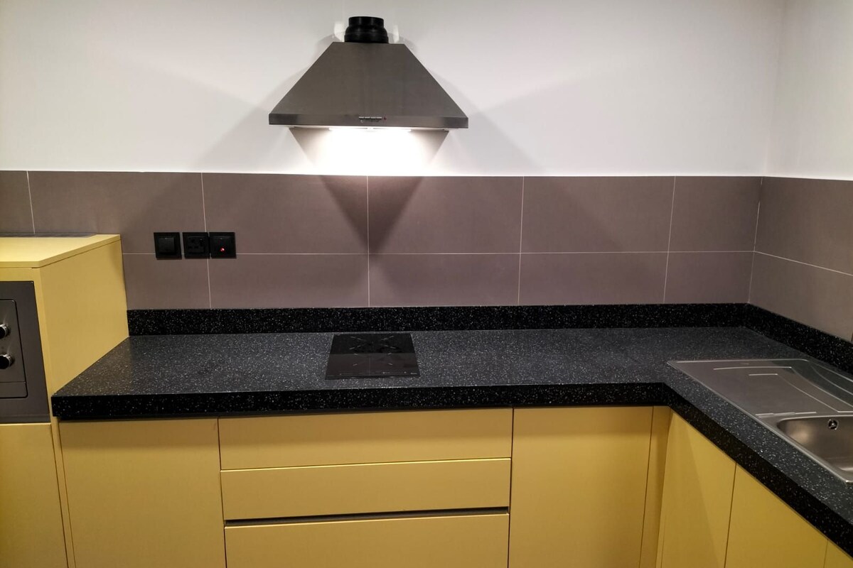 A kitchen with a black countertop, stainless steel sink, and yellow cabinets.