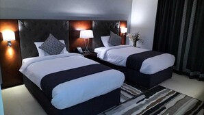 Une chambre d’hôtel avec deux lits, une tête de lit sombre, des lampes de chevet, un téléphone et un tapis à motifs.