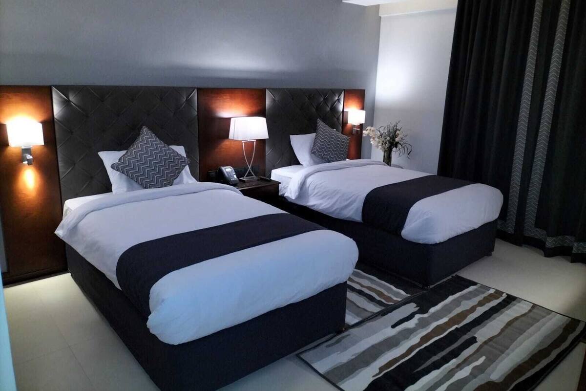 A hotel room with two beds, a dark headboard, bedside lamps, a telephone, and a patterned rug.
