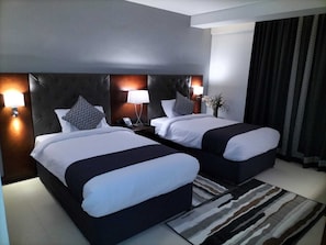 A hotel room with two beds, a dark headboard, bedside lamps, a telephone, and a patterned rug. - Tulip Inn Majan Hotel (Salalah)