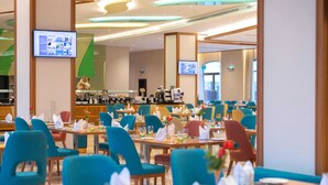 A hotel dining area with multiple tables and chairs, a buffet counter, and two televisions mounted on the walls. - Tulip Inn Majan Hotel (Salalah)