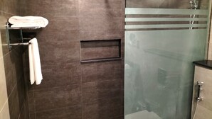 A modern bathroom with a glass shower enclosure, a towel rack, and a glass partition. - Tulip Inn Majan Hotel (Salalah)
