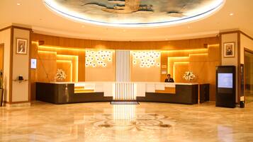 A hotel reception area with a central desk, a ceiling mural, and a polished marble floor.