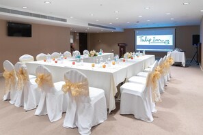 A conference room with a long table, white chairs with gold sashes, and a screen displaying 'Tulip Inn'. - Tulip Inn Majan Hotel (Salalah)