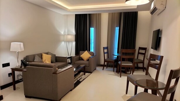 A modern hotel room with a sofa, chairs, a small table, a lamp, and a television. - Tulip Inn Majan Hotel (Salalah)
