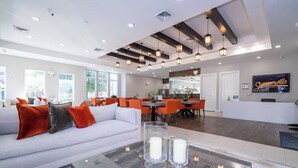 Eine geräumige Hotelhalle im modernen Design, mit einem weißen Sofa mit orangefarbenen und grauen Kissen, einem Essbereich mit orangefarbenen Stühlen und einem Empfangstresen.