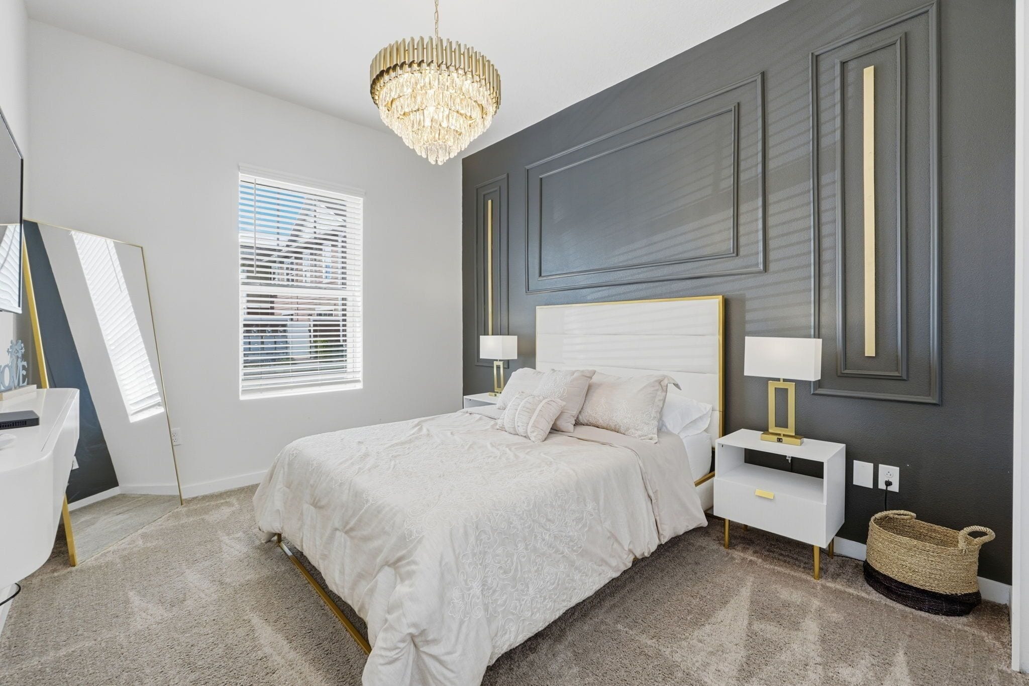 A bedroom with a bed, bedside tables, a chandelier, a window with blinds, and a wall with paneling.