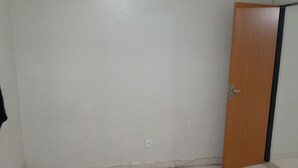 A room with white tiled flooring, a wooden door, and a white wall with a visible electrical outlet. - M norte  (Taguatinga)