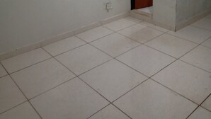 A room with white tiled flooring, a wooden door, and a light switch on the wall. - M norte  (Taguatinga)