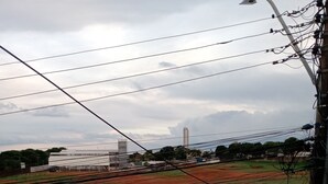 A view of a parking lot with a white car, a road, and a field with a building in the background. - M norte  (Taguatinga)