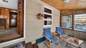 Un interior de madera con techo de madera, un ventanal grande y dos sillas azules con una mesa y una cesta.