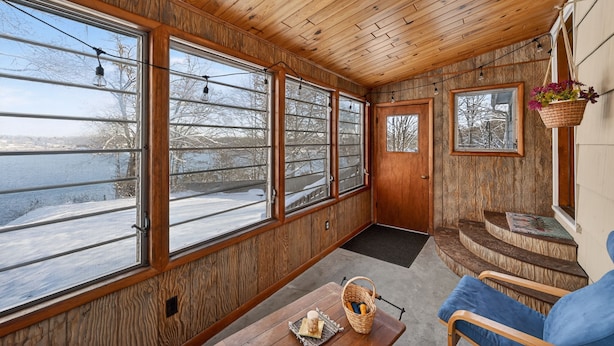 Interior acogedor de una cabaña con amplias ventanas, paredes de madera, un banco y una cesta con pan.