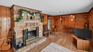 Un salón acogedor con chimenea de piedra, paredes de madera, un televisor y una guitarra.