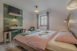 Een slaapkamer met een bed, een wandtelevisie, een raam met gordijnen en een nachtkastje met een lamp.